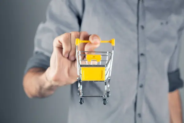 Bir Adam Elinde Bir Arabası Tutuyor Gri Arka Planda Alışveriş — Stok fotoğraf