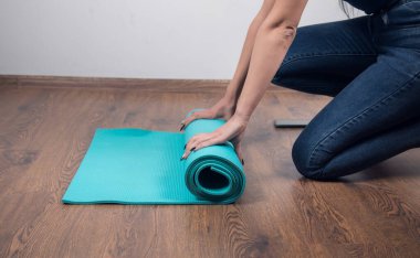 Kadın yerde yoga minderi topluyor.