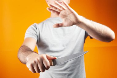 Bir adam elinde bıçakla turuncu bir arka planda duruyor.