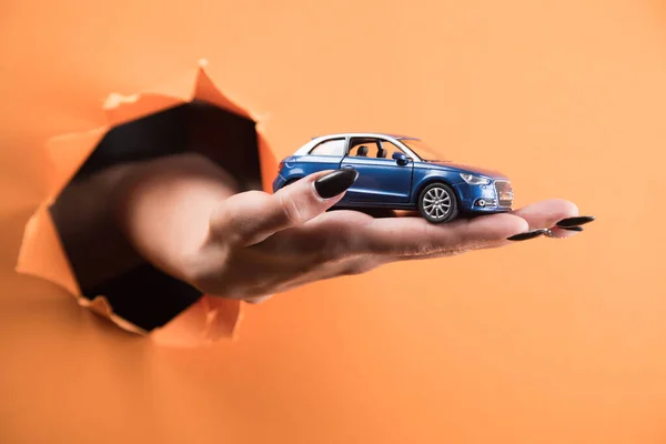 Weibliche Hand Hält Ein Spielzeugauto Auf Orangefarbenem Hintergrund — Stockfoto