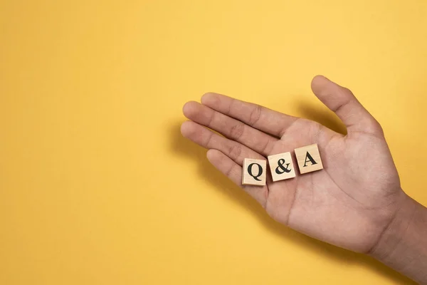 Q ve tahta alfabe fayanslarını gösteren bir el. Sorular ve Cevaplar desteği kavramı