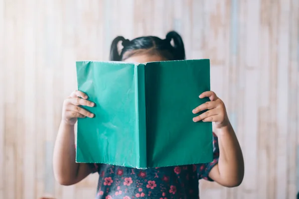 At kuyruklu küçük kız yüzünü örterken kitap okuyor. Erken eğitim, hobi ve çocukluk kavramı
