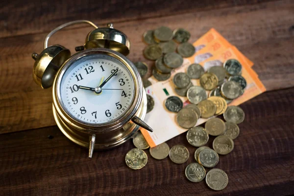 time is money concept - golden bell clock,money and coins on a wooden table background