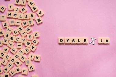 Üzerinde DYSLEXIA kelimesi olan alfabe kiremitleri pembe arka planda. Disleksi farkındalığı ve insan beyni gelişimi kavramı