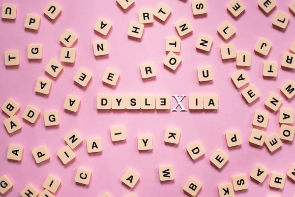 Üzerinde DYSLEXIA kelimesi olan alfabe kiremitleri pembe arka planda. Disleksi farkındalığı ve insan beyni gelişimi kavramı