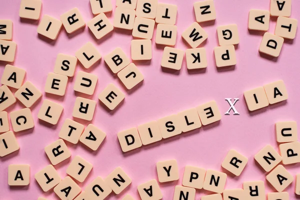 Üzerinde DYSLEXIA kelimesi olan alfabe kiremitleri pembe arka planda. Disleksi farkındalığı ve insan beyni gelişimi kavramı