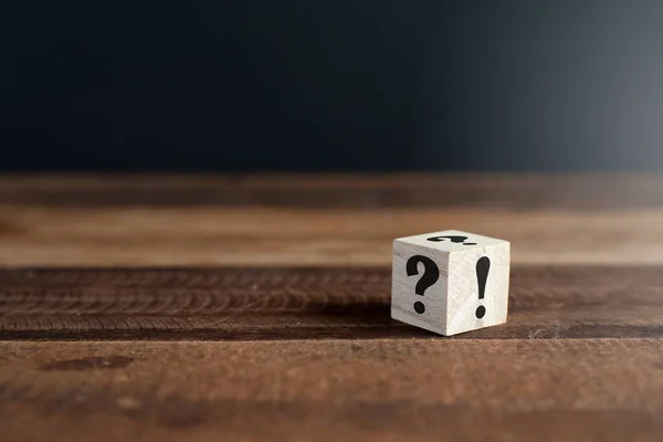 Tahta kübün üzerinde soru işareti ve ünlem işareti var. Belirsizlik, faq ve sorular ve cevaplar kavramı