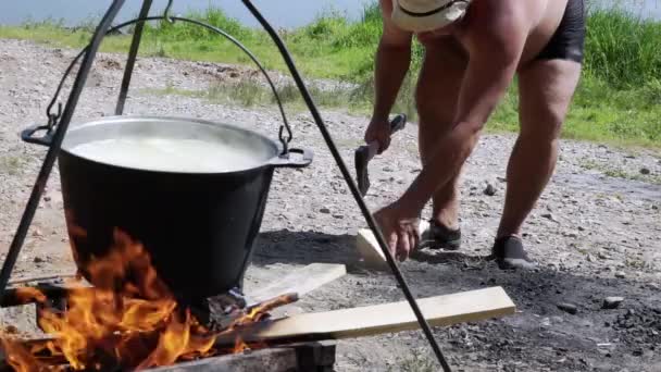 Un uomo che taglia legna sullo sfondo di una pentola su un fuoco — Video Stock