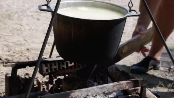 Um homem cortando madeira no fundo de uma panela em uma fogueira — Vídeo de Stock