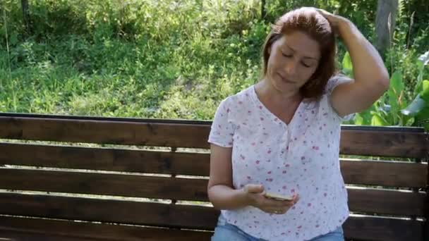 Een vrouw kijkt in een smartphone, swingen op een schommel in de tuin. — Stockvideo