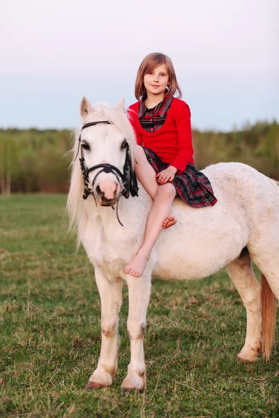 Pequena menina sentada montar um cavalo branco e sorrindo — Fotografia de Stock