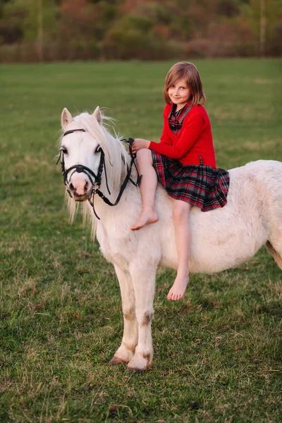 Little young girl in dress sitting on a pony riding Lady — Stock Photo, Image