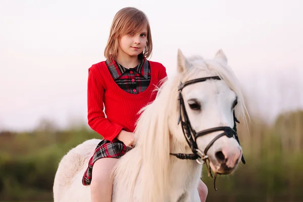 Petite fille assise sur un cheval dans une robe et regardant dans la caméra — Photo