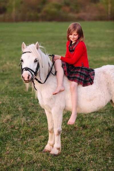 Bambina siede a cavallo di un cavallo bianco e guardando giù — Foto Stock