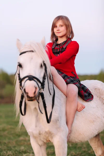 Kırmızı elbiseli küçük kız çocuk beyaz bir at ata biner gibi oturur — Stok fotoğraf