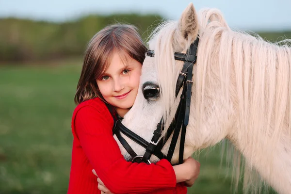 Menina pequena em um vestido vermelho abraçando sua cabeça um cavalo branco — Fotografia de Stock