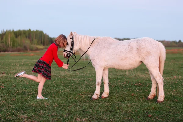 Klein model van een jong meisje zet haar kind in een kleine witte pony — Stockfoto