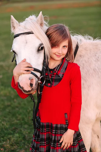 Menina pequena criança abraçando um pônei branco em sua cabeça e sorrindo — Fotografia de Stock