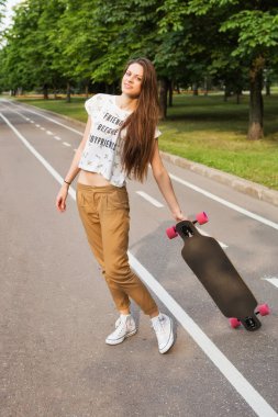 Güzel genç kız öğrencinin ayakta ve parkta yolda bir longboard tutarak uzun saçlı. Kaykay. Açık havada