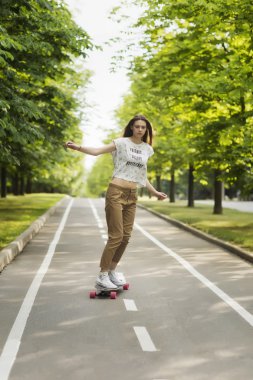 Trendy genç kadın açık havada yaz aylarında bir parkta bir yolda bir longboard gidiyor. Kaykay. Açık havada,
