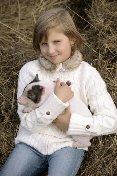 La niña en una blusa blanca se sienta y sostiene un lechón y sonríe. Retrato de estilo de vida —  Fotos de Stock