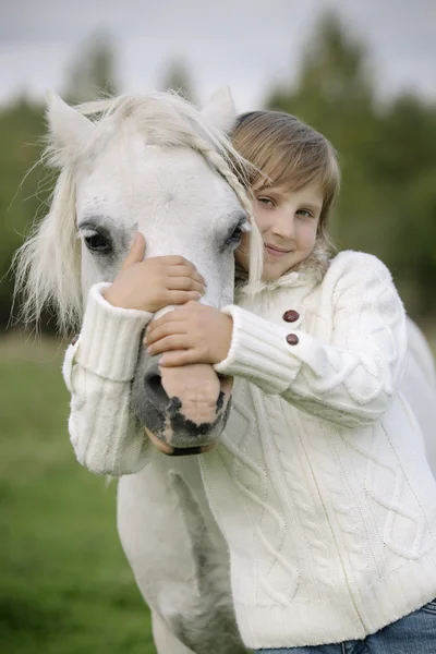 Young little girl embraces a white horse over the head. Lifestyle portrait — Stock Photo, Image