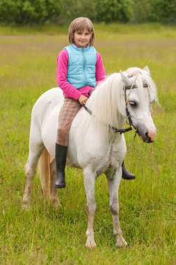 Ata biner gibi bir beyaz atın üzerinde oturanbir ve açık havada gülümseyen genç kız çocuk