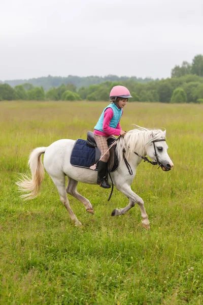 Belle petite fille sur un cheval blanc galopant à travers le champ En plein air — Photo