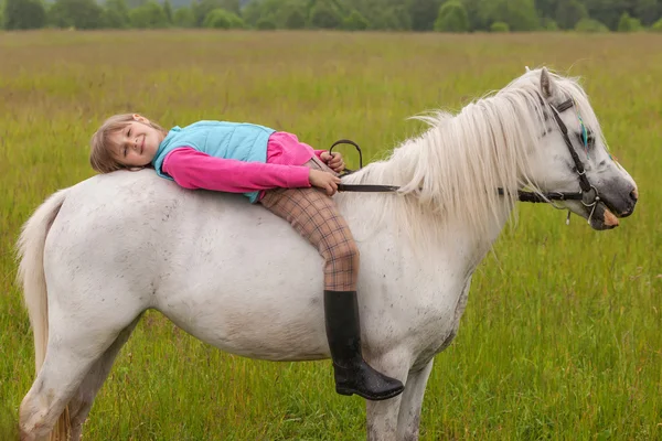 Het kleine meisje lag op haar rug wit paard en glimlachend Outdoors — Stockfoto