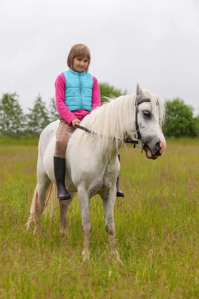 Dziecko dziewczynka siedzi okrakiem białego konia i uśmiechając się na zewnątrz — Zdjęcie stockowe