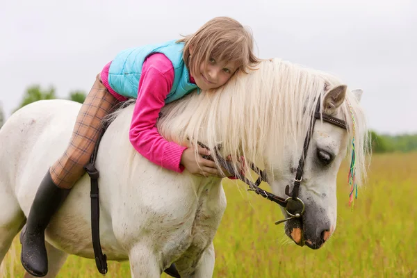 La jeune fille s'allonge sur le dos du cheval blanc et sourit en plein air — Photo