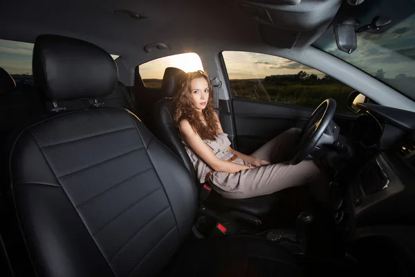 Beautiful young girl sitting in a car and looking at the camera outdoors — Stock Photo, Image