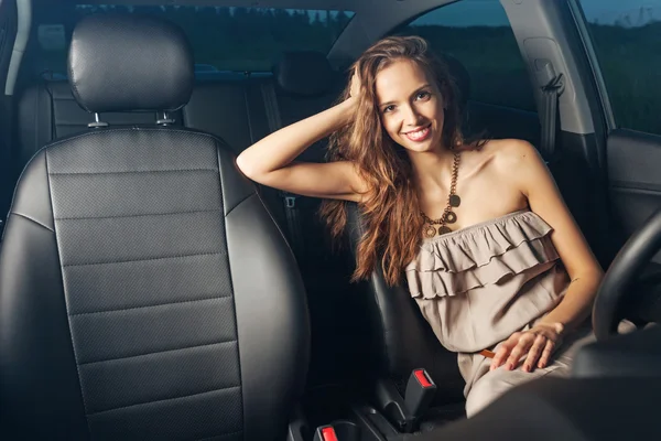 Menina sexy bonita sentada ao volante de um carro e sorrindo ao ar livre — Fotografia de Stock