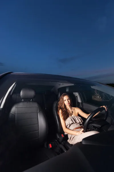 A young girl with beautiful hair and dress sitting behind the wheel of a car — Stock Photo, Image