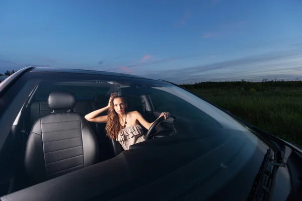 Молодая сексуальная женщина, сидящая за рулем машины и смотрящая в камеру на улице — стоковое фото