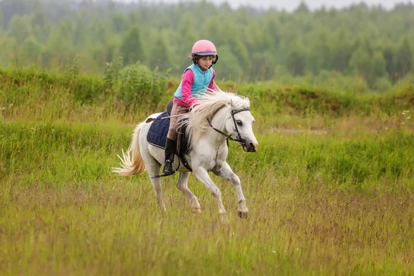 Little baby girl confident riding a horse at a gallop across the field — Stock Photo, Image