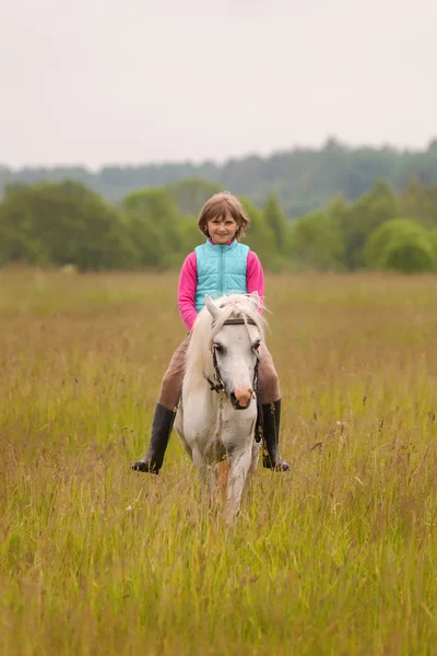 Klein kind rijden op een wit paard en glimlachend Outdoors — Stockfoto