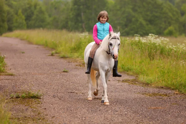 Klein kind rijden op een wit paard op de weg buiten — Stockfoto