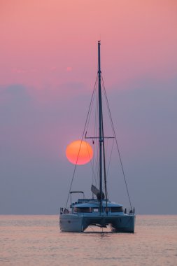Denizin üzerinde yükselen güneşin arka plan üzerinde katamaran Yelken