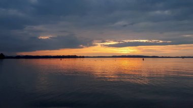 Chiemsee Gölü 'nde gün batımı Yazın bulutlu gökyüzüne karşı suda yansıyan yansımalarla