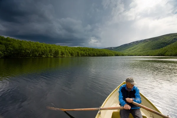 Pescatore senior che rema in barca su un lago Mikkeljavre a Norwa Immagine Stock
