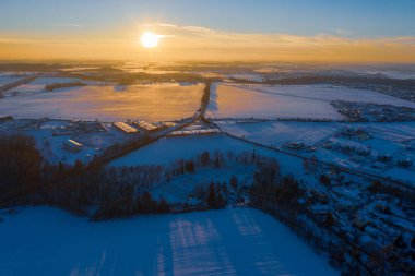 Beyaz karlar üzerinde kış günbatımının havadan görünüşü ve uzun gölgeli ağaçlar.