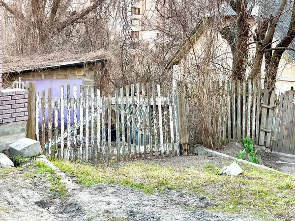 木製のみすぼらしいフェンスの後ろに古い放棄された家 家の前に白い柵 街中に捨てられた場所 — ストック写真