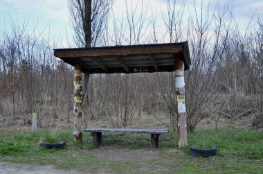 Eski bir köyde ahşap bir otobüs durağı. Otobüs durağında dinlenmek için ahşap bir bank. Yedek kulübesinde. Eski durak ve eski dükkan. Yol kenarında ıssız bir yer..