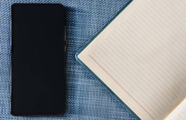 Mavi arkaplanda akıllı telefon ve defter