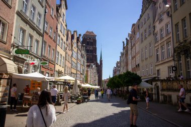 Polonya 'nın Gdansk kentindeki canlı Mariacka Caddesi' nin arka planında renkli cepheleri, turistleri, açık hava kafeleri ve St. Mary Kilisesi var. 20 Haziran 2024. Gdanks - Polonya