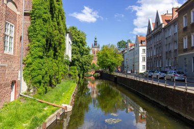 Polonya 'nın Gdansk kentindeki huzurlu kanal manzarası tarihi mimarisi, yemyeşil yeşilliği ve mavi gökyüzünün altındaki kilise kulesiyle