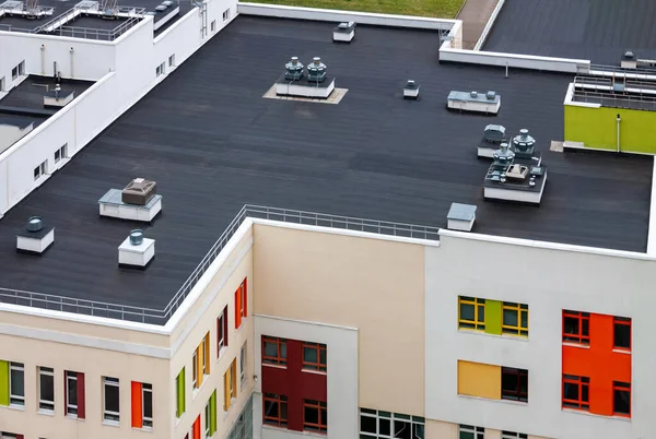 Modern bir apartmanın tepesinde havalandırma ve su yalıtım zarları olan düz çatı, sarı yeşil kırmızı bina..
