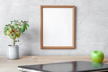 Beyaz portre çerçeveli bir işyeri, dizüstü bilgisayar, sulu ot, vejetaryen aperatif yeşil elma masa gri beton duvar arka planında. İskandinav iç mimarisi. Çalışma alanı ofis kavramı.