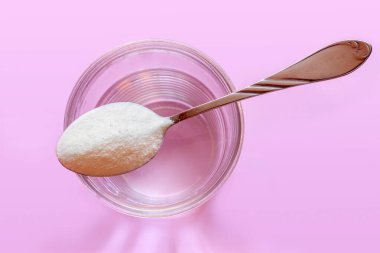 Yakın plan düz kolajen tozu kaşığı ve cam su pembe renk arka plan içerir. Sürdürülebilirlik, güzellik ve sağlıklı yaşam konsepti